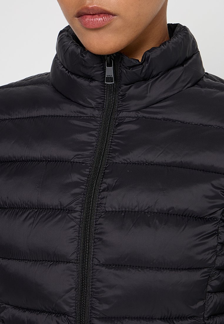 Schwarze gepolsterte Jacke mit hohem Kragen, ausgestattet mit einem Reißverschluss vorne und gestepptem Design. Glatte Textur mit leichtem Glanz.