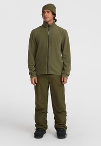 Giacca in pile verde oliva con collo alto e chiusura a zip, abbinata a pantaloni cargo coordinati e stivali da neve neri. Design minimalista.