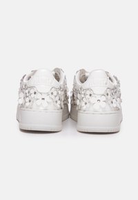 Zapatillas blancas con aplicaciones florales en relieve y tachuelas plateadas que cubren el talón y los laterales, con un logotipo en relieve en la parte posterior.