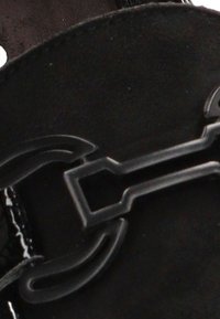 Sandalia negra con un acabado de cuero liso, con un llamativo hebilla metálica y una plantilla texturizada para mayor comodidad.