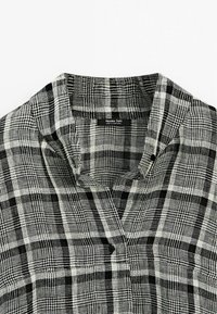 Karierter Hemd mit einem schwarz-weißen Schottenmuster, Kragen, Knopfdetails, gefertigt aus leichtem Stoff mit weicher Textur.