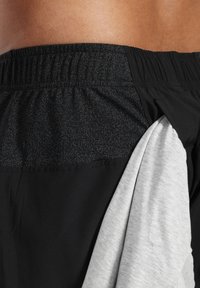 Svarta sportshorts med en texturerad elastisk midjeband, med en grå innerfoder som är något synlig från sidan.