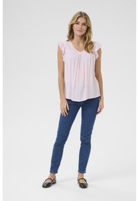 Helles pinkes Bluse mit Rüschenschultern, gerafftem Halsausschnitt, kombiniert mit dunkelblaunen Skinny Jeans und schwarzen Ballerinas. Geschmeidiger, leichter Stoff.