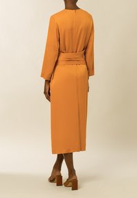 Vestido naranja de manga larga, con cintura ceñida, silueta recta y tela suave. Presenta un discreto cierre de cremallera en la parte posterior y longitud a media pantorrilla.