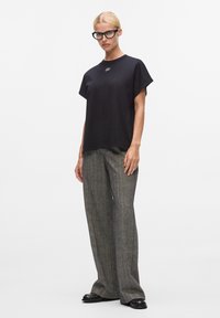 Schwarzes kurzärmliges T-Shirt mit Rundhalsausschnitt und gesticktem Detail; kombiniert mit grauen hochgeschnittenen Hosen mit strukturiertem Muster.