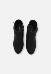 Schwarze Stiefeletten aus Wildleder mit glatter Textur, ausgestattet mit einem seitlichen Reißverschluss und einem kleinen goldenen Akzent in der Nähe des Knöchels.