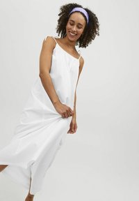 Robe blanche fluide avec de fines bretelles et des fentes sur les côtés. Fabriquée en tissu léger, elle présente une coupe ample et décontractée.