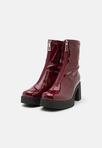 Botines de charol burdeos con dos cremalleras frontales, suela de plataforma negra robusta y un acabado liso y brillante.