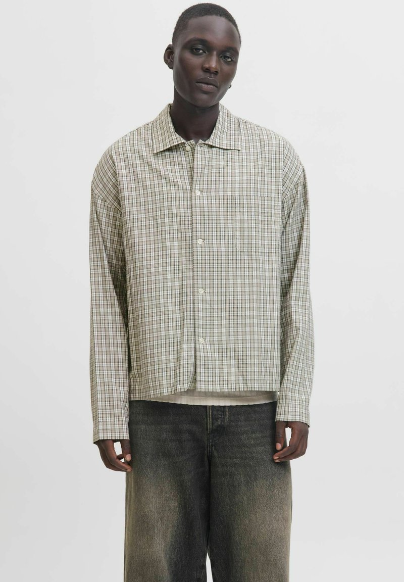 Leichte, karierte Button-Down-Bluse mit grünen, braunen und weißen Farbtönen, entspannter Schnitt und einer Brusttasche. Über dunkler Jeans getragen.