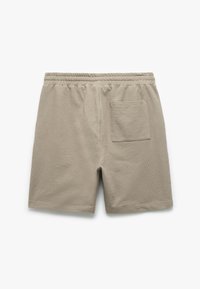 Pantaloni corti leggeri beige realizzati in tessuto testurizzato, con vita elasticizzata e una tasca sul retro. Finitura liscia, design che arriva fino al ginocchio.