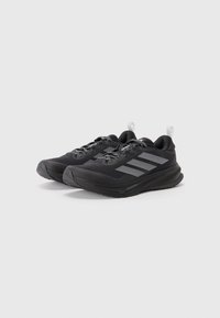 Baskets de sport noires avec un dessus en mailles, des rayures grises réfléchissantes et une semelle en caoutchouc texturé. Comprend des lacets et une languette pour un enfilage facile.