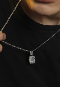 Strieborný náhrdelník s retiazkou, ktorý zdobí obdĺžnikový prívesok, ozdobený textúrovaným písmenkovým dizajnom a posiaty malými krištáľmi pre detaily.