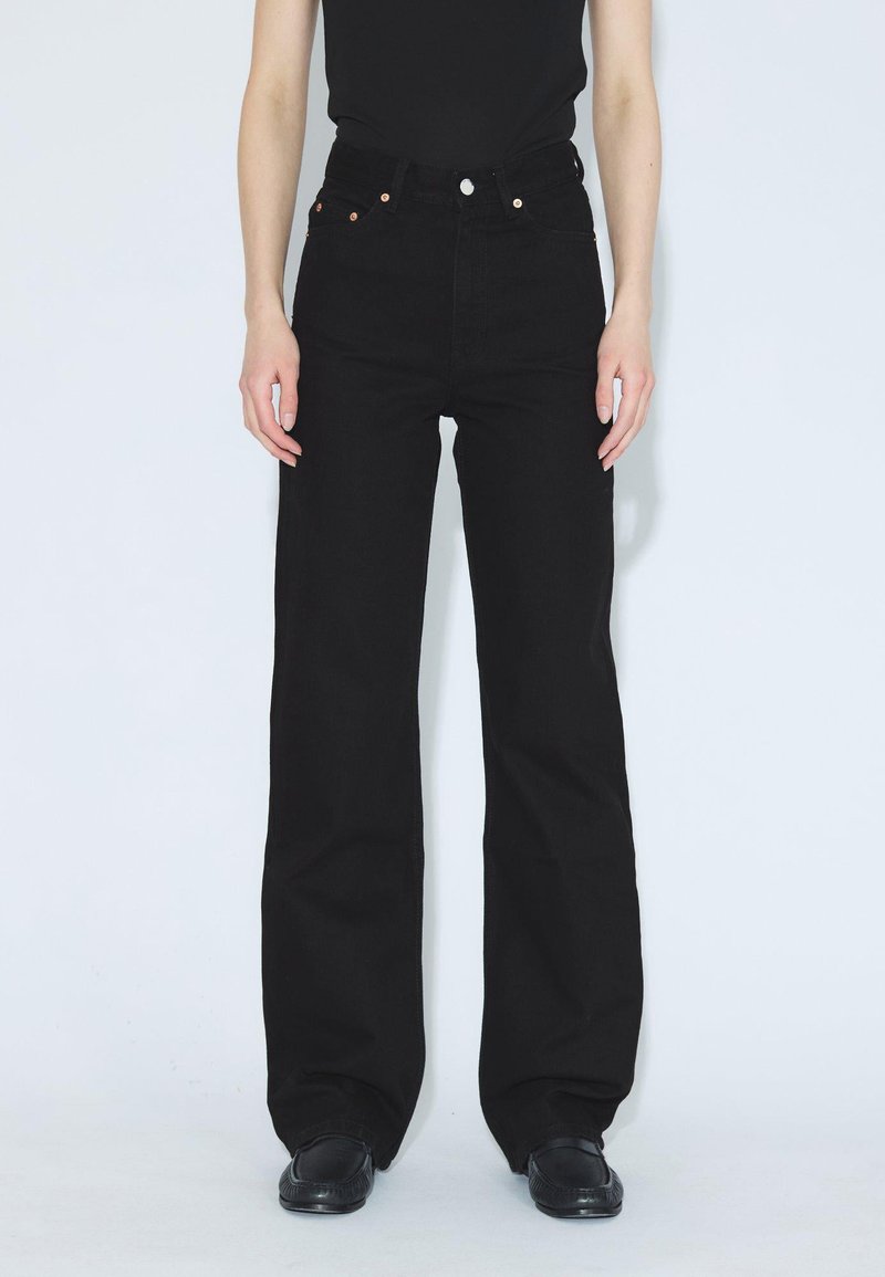 Jeans negros de tiro alto hechos de denim, con corte recto, herrajes de botón de cobre y sin patrones o adornos visibles.