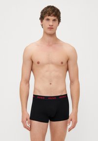 Boxer brevi neri in cotone, con una vita elastica rossa riportante il logo "HUGO". Progettati per una vestibilità aderente con una gamba di lunghezza media.