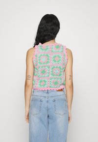 Crochet top in green, pink, and blue squares with scalloped edges. Worn with high-waisted light blue jeans, showcasing a textured design.