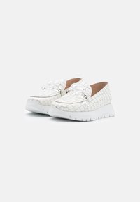 White slip-on shoes with a textured grid pattern, featuring a bow on the front and a white rubber sole, highlighting a minimalist design.