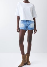 Bílý zkrácený tričko, ošuntělé světle modré džíny s třepeným lemem a béžové semišové kotníkové boty s vyšívanými detaily.