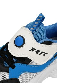 Chaussure de sport bleu, blanc et noir avec tissu en maille, lacets noirs, un bouton rond bleu sur une bride blanche, et « BRK » imprimé sur la bride.