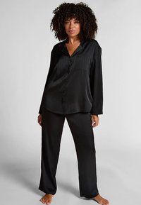 Zwart satijnen pyjamaset met een blouse met knopen en lange mouwen met een lichte glans en bijpassende loszittende broek. Eenvoudig, gestructureerd ontwerp.