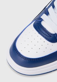 Λευκό και ναυτικό αθλητικό παπούτσι με λείο δερμάτινο επάνω μέρος, διατρημένη περιοχή στα δάχτυλα, επίπεδα λευκά κορδόνια και κομψή σόλα από καουτσούκ.