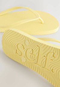 Gele rubberen slippers met een gestructureerde voetbed en een verhoogde merknaam "self." Dunne banden en een golvend zoolpatroon voor grip en comfort.