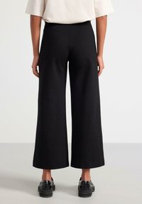Svarta vida byxor med hög midja, tillverkade av ett smidigt, elastiskt tyg. Har en rak skärning, ankle-length design och subtil textur.