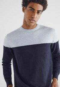 Sweter dzianinowy z jasnoszarym górnym fragmentem i ciemnoniebieskim dolnym fragmentem. Żebrowany okrągły dekolt i mankiety, gładka tekstura. Prosty, nowoczesny design.
