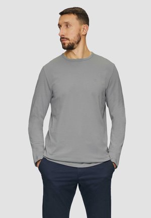 Grijze lange mouwen T-shirt met een ronde halslijn en een subtiele logo op de borst. Glad materiaal, ontspannen pasvorm, gecombineerd met donkere broeken.