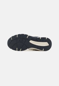 Talpa de sneaker din cauciuc negru, cu modele texturate pentru aderență, forme curbate și accente de culoare crem. Prezintă logo-ul brandului pe mijlocul talpii.