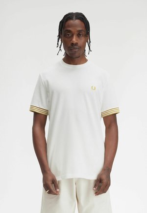 T-shirt bianco a maniche corte con polsini a righe dorate a coste e un piccolo logo dorato sul petto. Tessuto leggero con una texture liscia.