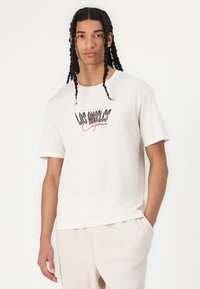 Crème-kleurige katoenen T-shirt met een grafisch ontwerp met de tekst "LOS ANGELES California." Korte mouwen en een relaxte pasvorm.