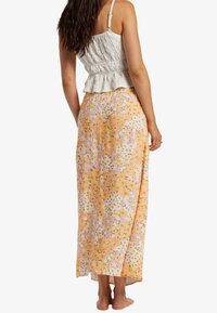 Top de peplum en tejido blanco, combinado con una falda larga y fluida de color naranja con un patrón floral en rosa y verde. Textura suave, ajuste casual.