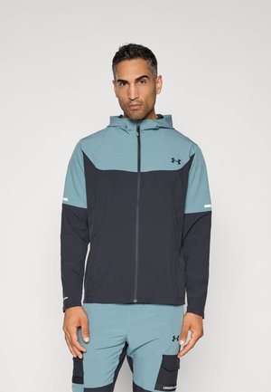 Chaqueta con capucha que presenta un diseño bicolor con una parte superior en azul claro y una parte inferior en azul oscuro, fabricada en un tejido ligero y texturizado.
