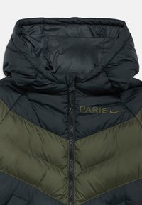 Casaco tipo puffer com design em chevron preto e verde-oliva, com fecho de correr frontal e capuz, realçado com "PARIS" e logo da Nike em bordado dourado.