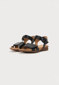 Black leather sandals with adjustable ankle straps, open-toe design, cushioned insole, and a brown rubber sole. Features stitching detail.