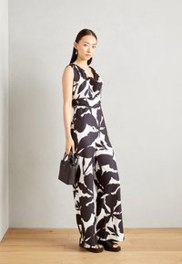 Mono de flores en blanco y negro con cuello de drapeado, piernas amplias y cintura ajustada, combinado con un pequeño bolso negro y sandalias de plataforma.