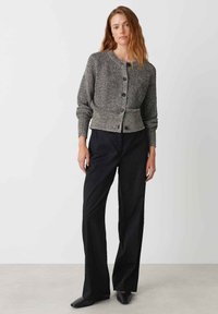 Cardigan grigio lavorato a maglia con scollo rotondo, bottoni frontali e polsini a costine, abbinato a pantaloni neri a gamba larga e scarpe nere.