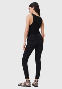 Top negro sin mangas combinado con pantalones cargo negros con camuflaje. Los pantalones cuentan con tobillos con cremallera y bolsillos traseros. Se llevan con sandalias de tiras metálicas.