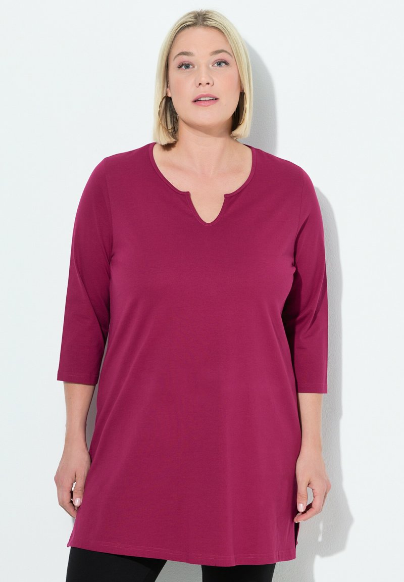 Maroon tunika huppari, joka on valmistettu pehmeästä kankaasta, jossa on V-pääntie ja kolmanneksen pituiset hihat, sekä sivuhalkiot liikkumisen helpottamiseksi.