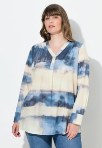 Lange mouw, V-hals shirt in crèmewit met blauwe aquarelstrepen. Met knoopsluiting, zachte stof en een ontspannen pasvorm.