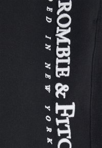 Tessuto nero con testo ricamato bianco "ABERCROMBIE & FITCH EST. 1892 NEW YORK" e una superficie texturizzata, che mette in risalto i dettagli del marchio.