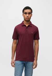 Bordowa koszulka polo z krótkimi rękawami, kołnierzykiem i dwuguzikową plisą. Z małym, wyszywanym logo na lewej piersi. Średniej grubości bawełna.