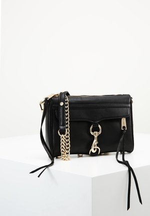 Sac bandoulière en cuir noir avec bandoulière chaîne dorée et détail de fermoir, placé sur un socle blanc sur un fond clair uni.
