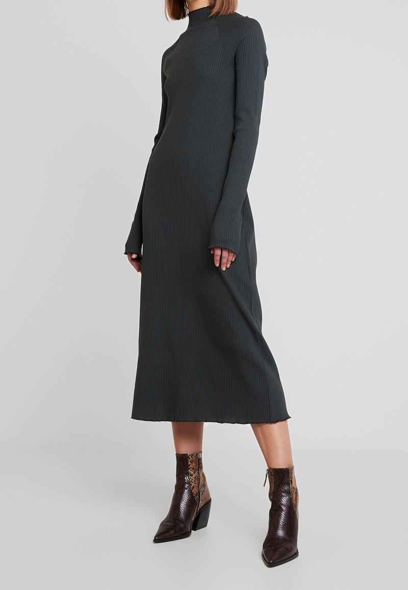 Ciemnoszara, prążkowana sukienka midi z długimi rękawami i wysokim kołnierzem; posiada surowe wykończenie. Połączona z teksturowanymi botkami za kostkę w ciemnym brązie w wężowy wzór.