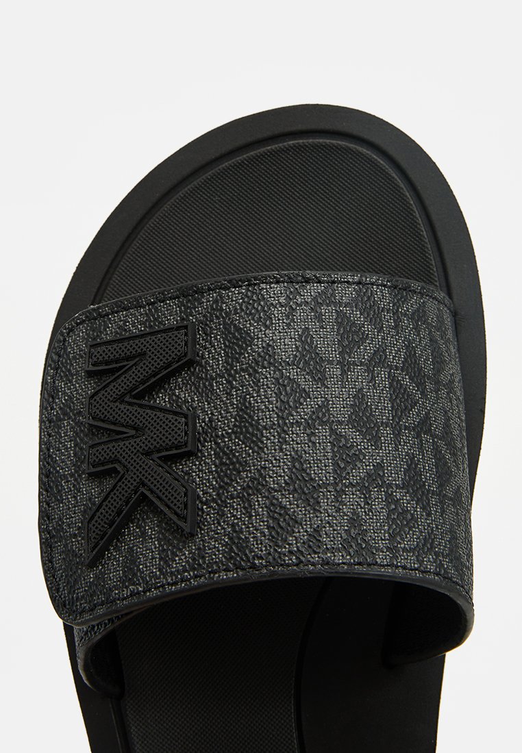 Sandalia negra de slide con tira de tela texturizada que presenta un sutil logo. La suela es de goma suave, proporcionando un contraste con el patrón de la tira.