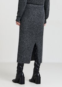 Jupe midi en maille gris foncé avec une fente au dos, associée à des bottes à talons noires brillantes montant jusqu'aux genoux. Texture douce et coupe ajustée.