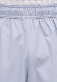 Tissu bleu clair avec une ceinture élastique et un détail de couture froncée, montrant la texture et de légères rides du tissu.