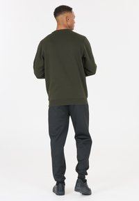 Sweatshirt vert olive avec une coupe décontractée, col rond et ourlet côtelé, associé à un pantalon de jogging noir fuselé et des baskets noires.