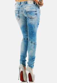 Slanke blauwe denim jeans met versleten details, voorzien van twee achterzakken, een logo-label en een slim fit. Gecombineerd met zilveren stilettohakken.