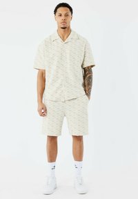 Chemise à manches courtes beige clair et short assorti, dotés d'un motif géométrique. Matériau en coton, coupe décontractée, associé à des baskets blanches.